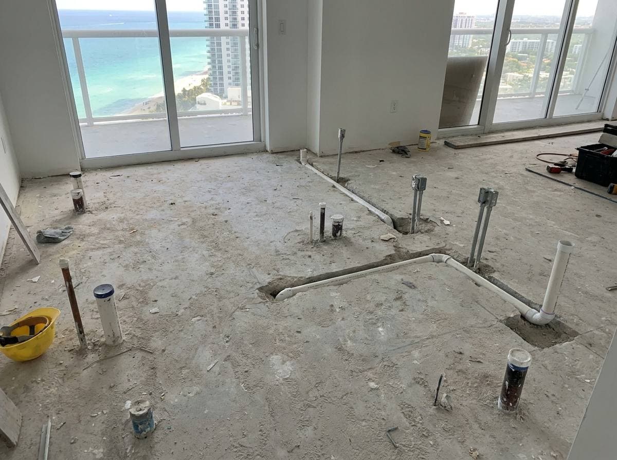 High-rise condo bathroom rough-in showing concrete floor slab with existing plumbing penetrations and limited drain re-route capacity