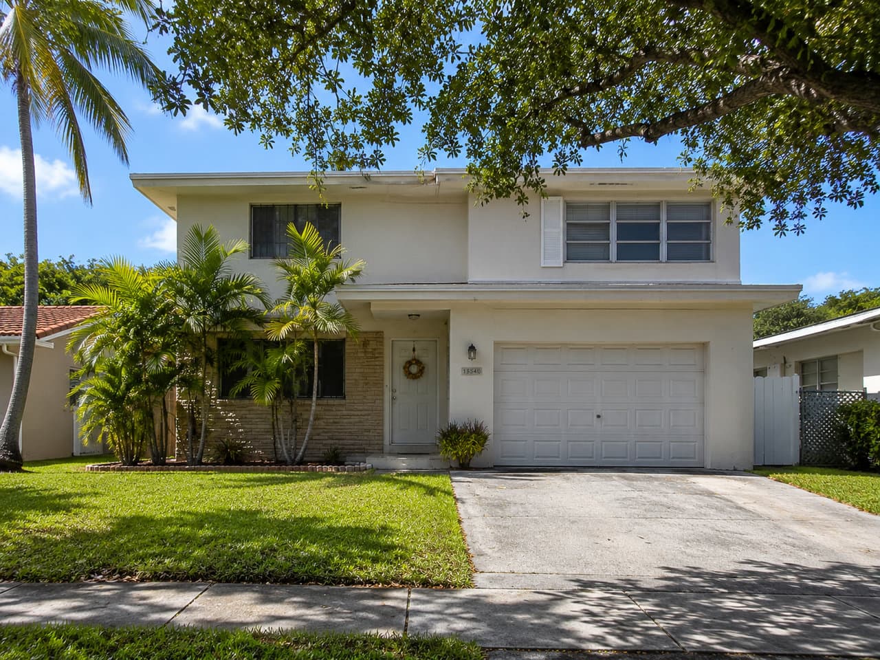 Two-story home with a stucco and stone-veneer facade, two-car garage and mature oak canopy