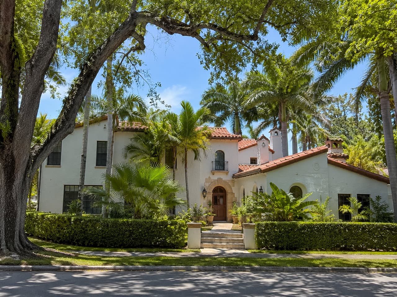 Two-story Mediterranean Revival home with white stucco, barrel-tile roof and an arched entry