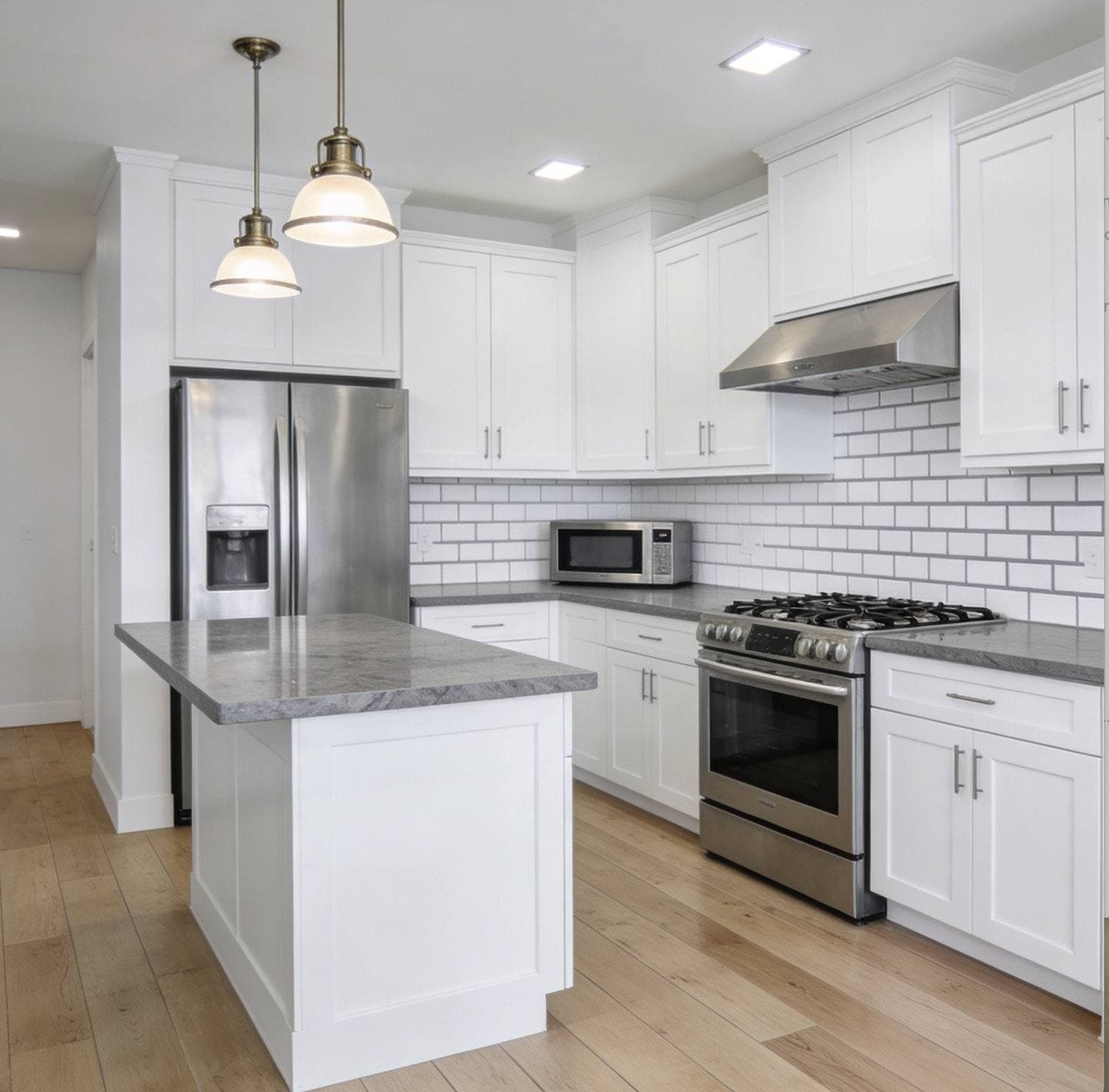 Completed kitchen remodel with white shaker cabinetry, a center island with pendant lighting, and stainless steel appliances