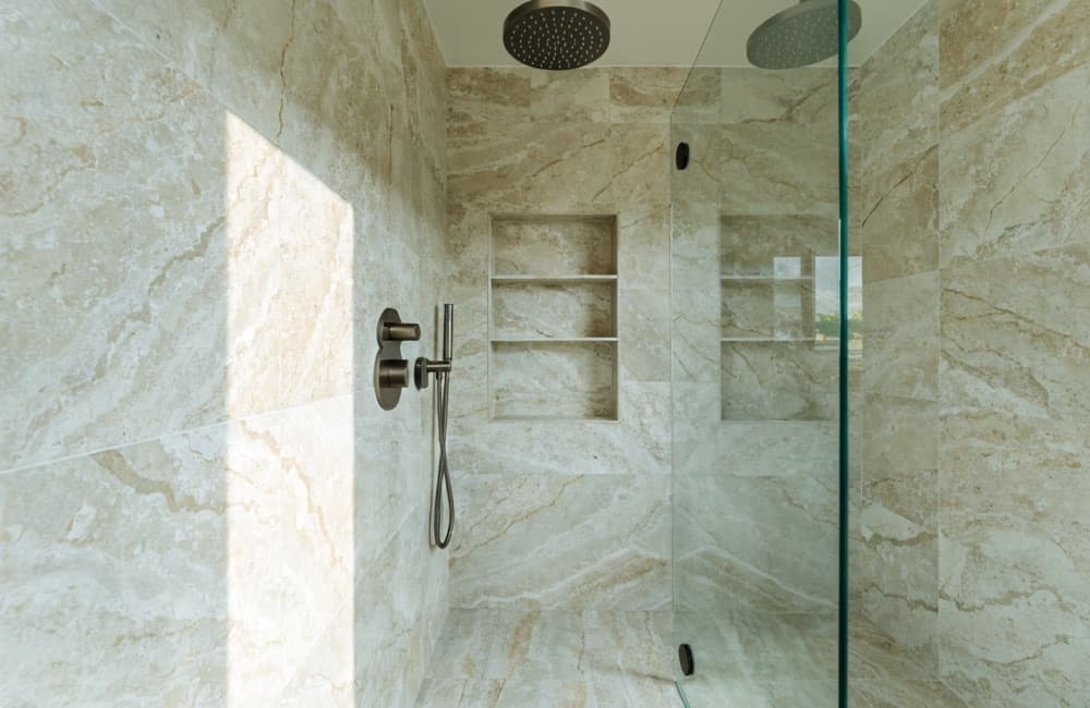 Walk-in shower finished in large-format stone-look tile, with a recessed niche, a handheld fixture and a frameless glass panel.