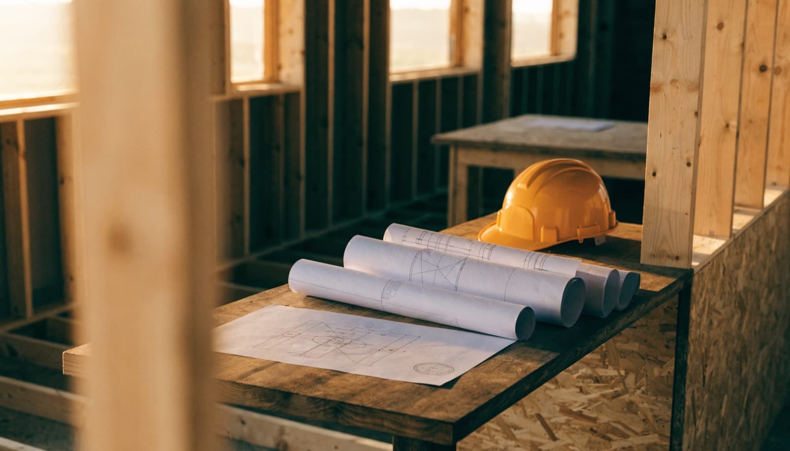 How long does a renovation permit take in Miami: rolled construction drawings and a hard hat on a plywood bench inside a wood-framed structure.